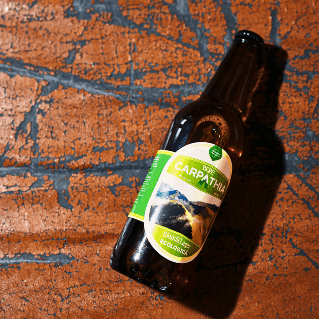 Sticlă de bere Pardon Carpathia artizanală, blondă ecologică 5% alcool, fotografiată pe fundal artistic texturat