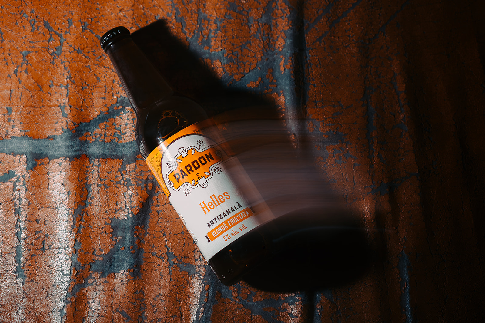 Sticlă de bere nefiltrată Pardon Helles artizanală, blondă fructată cu 5% alcool, fotografiată pe fundal artistic texturat