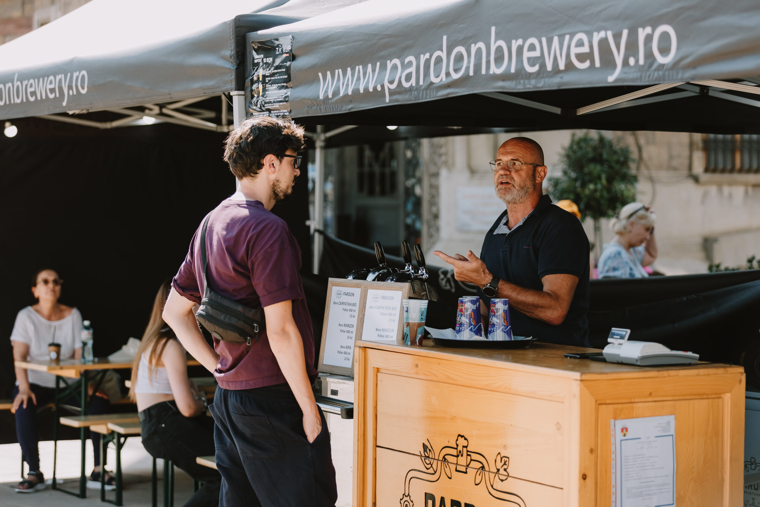 Doua persoane vorbesc la standul Pardon Brewery la evenimentul de bere artizanala nefiltrata Urbea